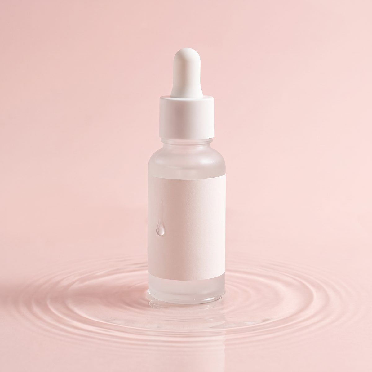Dropper bottle standing in rippling water on a pink backdrop